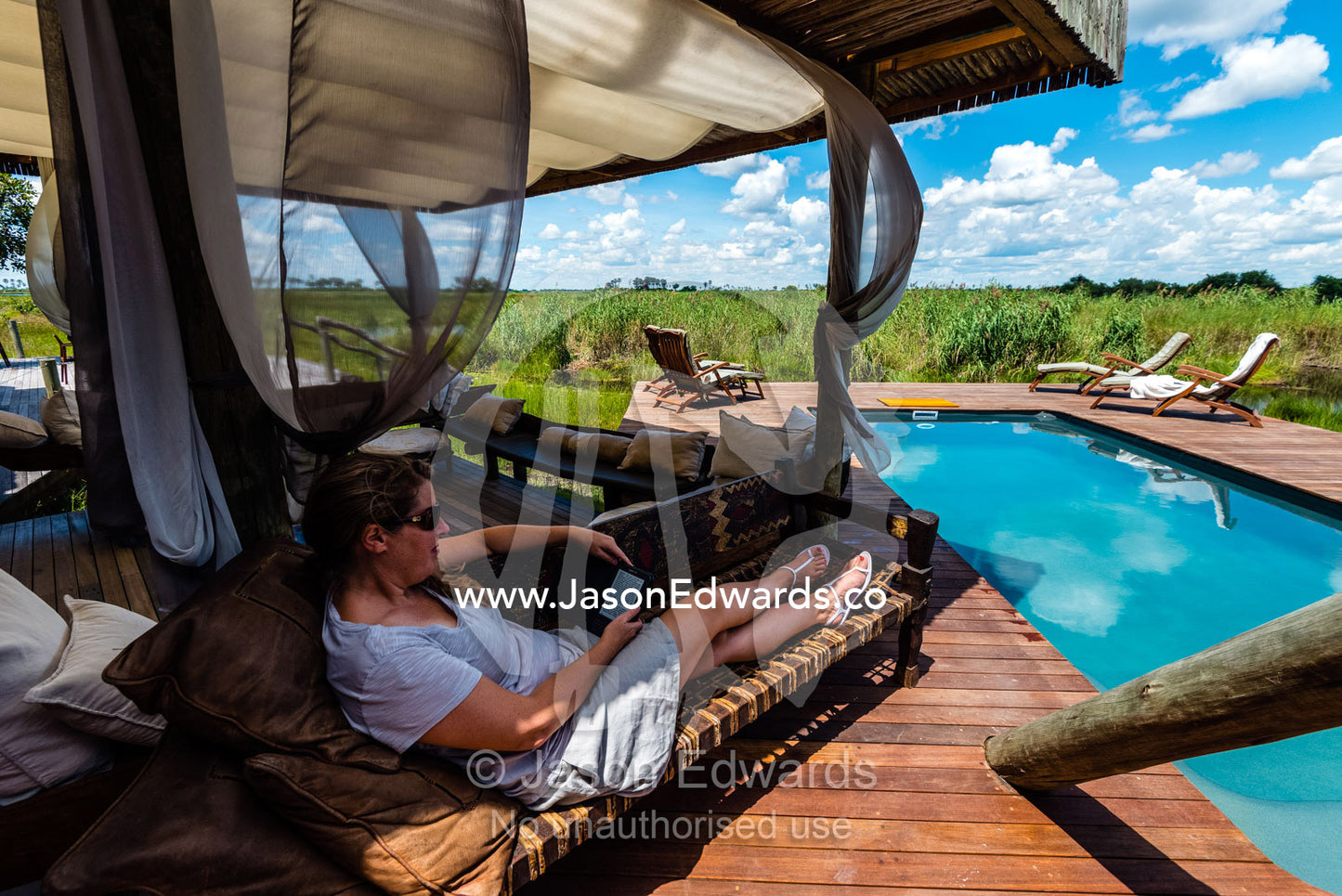 A woman relaxing and reading at a luxury safari camp. Selinda Camp, Selinda Reserve, Linyanti Region, Northern Botswana.