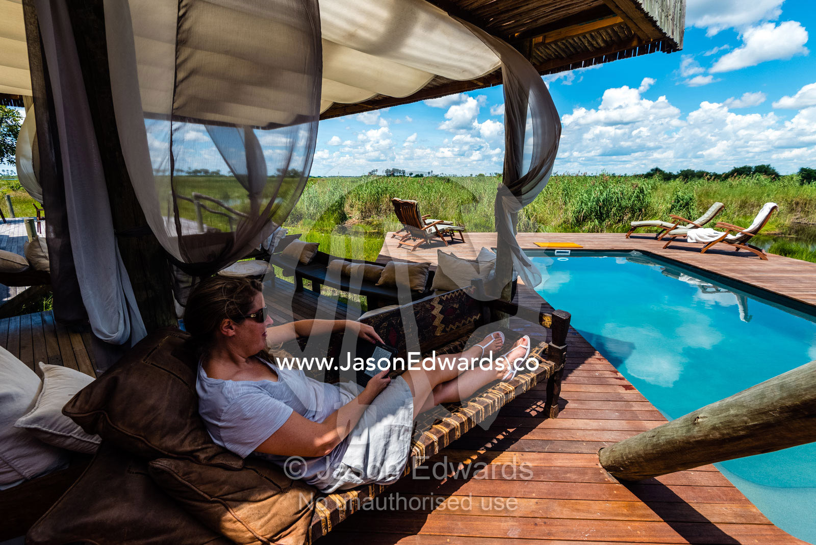 A woman relaxing and reading at a luxury safari camp. Selinda Camp, Selinda Reserve, Linyanti Region, Northern Botswana.