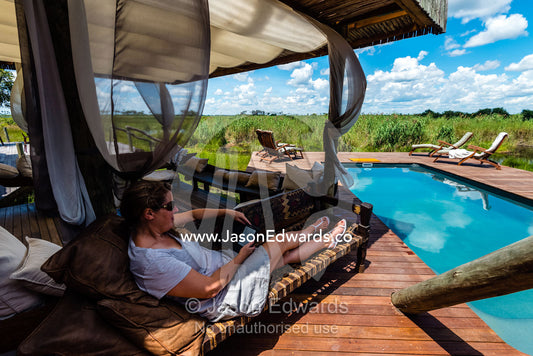 A woman relaxing and reading at a luxury safari camp. Selinda Camp, Selinda Reserve, Linyanti Region, Northern Botswana.