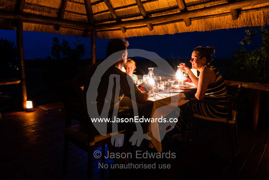 A family dining on the verandah of a luxury safari camp tent. Selinda Camp, Selinda Reserve, Linyanti Region, Northern Botswana.