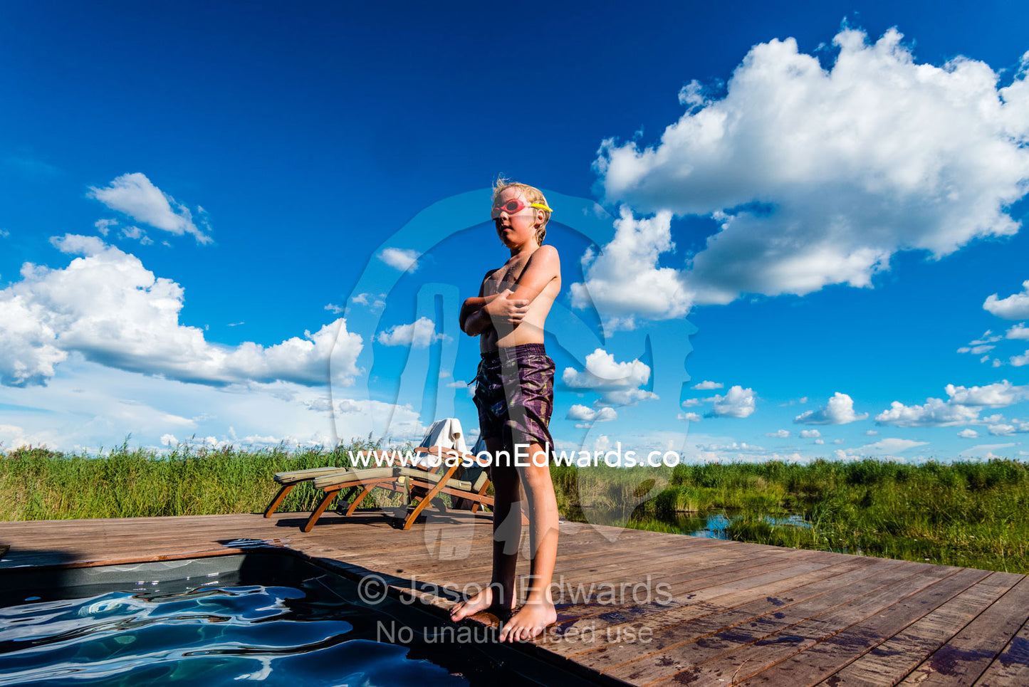 A boy standing on the side of a swimming pool in a luxury safari camp. Selinda Camp, Selinda Reserve, Linyanti Region, Northern Botswana.