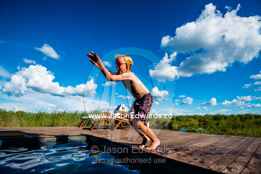 A boy jumping into a swimming pool in a luxury safari camp. Selinda Camp, Selinda Reserve, Linyanti Region, Northern Botswana.