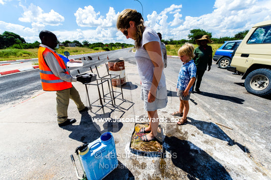 Tourists washing their shoes in antiseptic foot baths to prevent the spread of agricultural diseases. Kalahari Desert, Botswana.