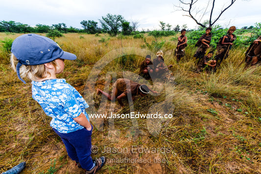 A boy watches a San Bushmen demonstrate hunting for antelope. Kalahari Desert, Botswana.