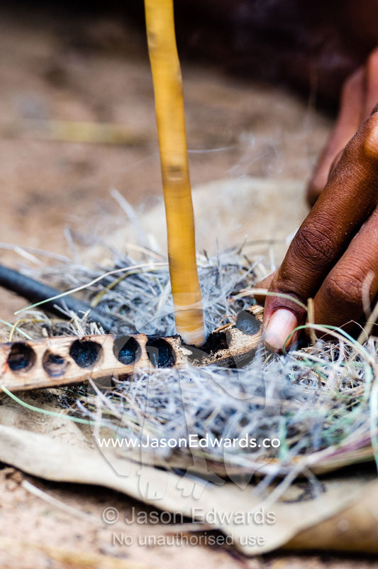San Bushmen starting a fire using dry grass kindling, a wooden drill of hard wood and a soft wood fire board. Kalahari Desert, Botswana.