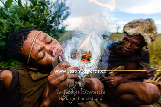 A San Bushmen blowing on a small flier he started using sticks. Kalahari Desert, Botswana.