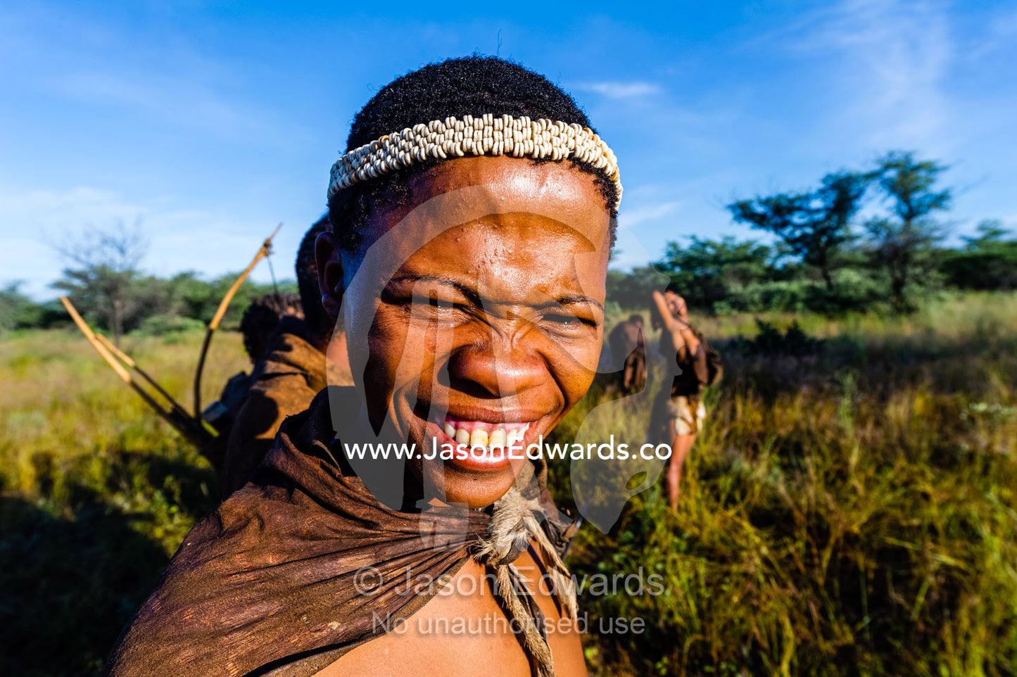 A young smiling San Bushmen wearing an Ostrich egg shell head band. Kalahari Desert, Botswana.