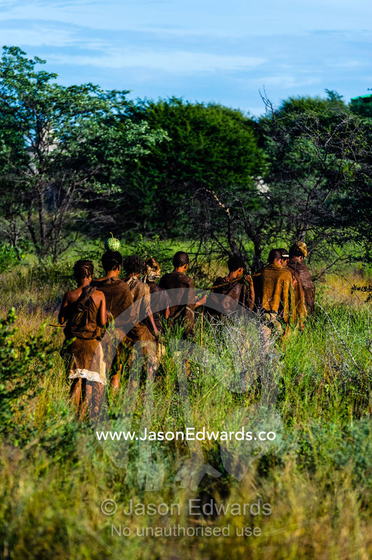 A family of San Bushmen in leather animal skins walking through a grassland at dawn. Kalahari Desert, Botswana.