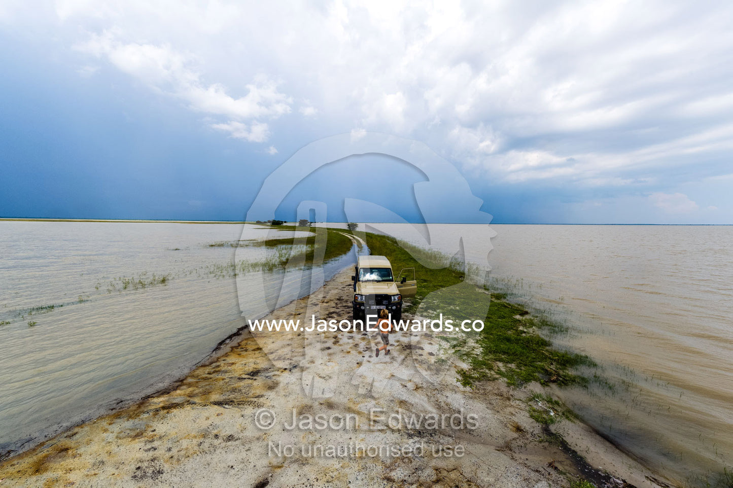 A boy running to a 4wd on a flooded salt pan. Makgadikgadi Pans, Botswana.