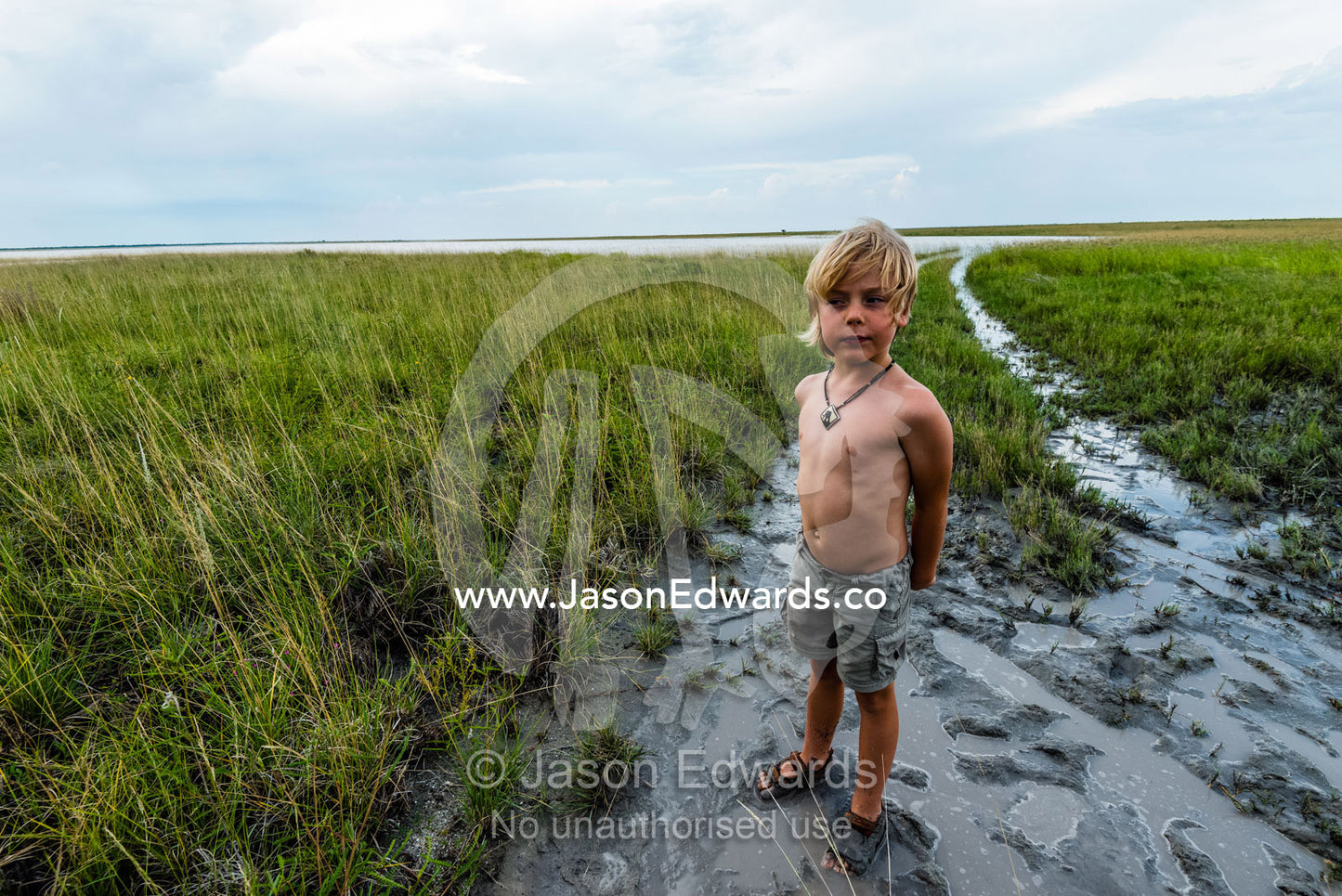 A boy on safari standing in the mud on a flooded savannah plain. Makgadikgadi Pans, Botswana.