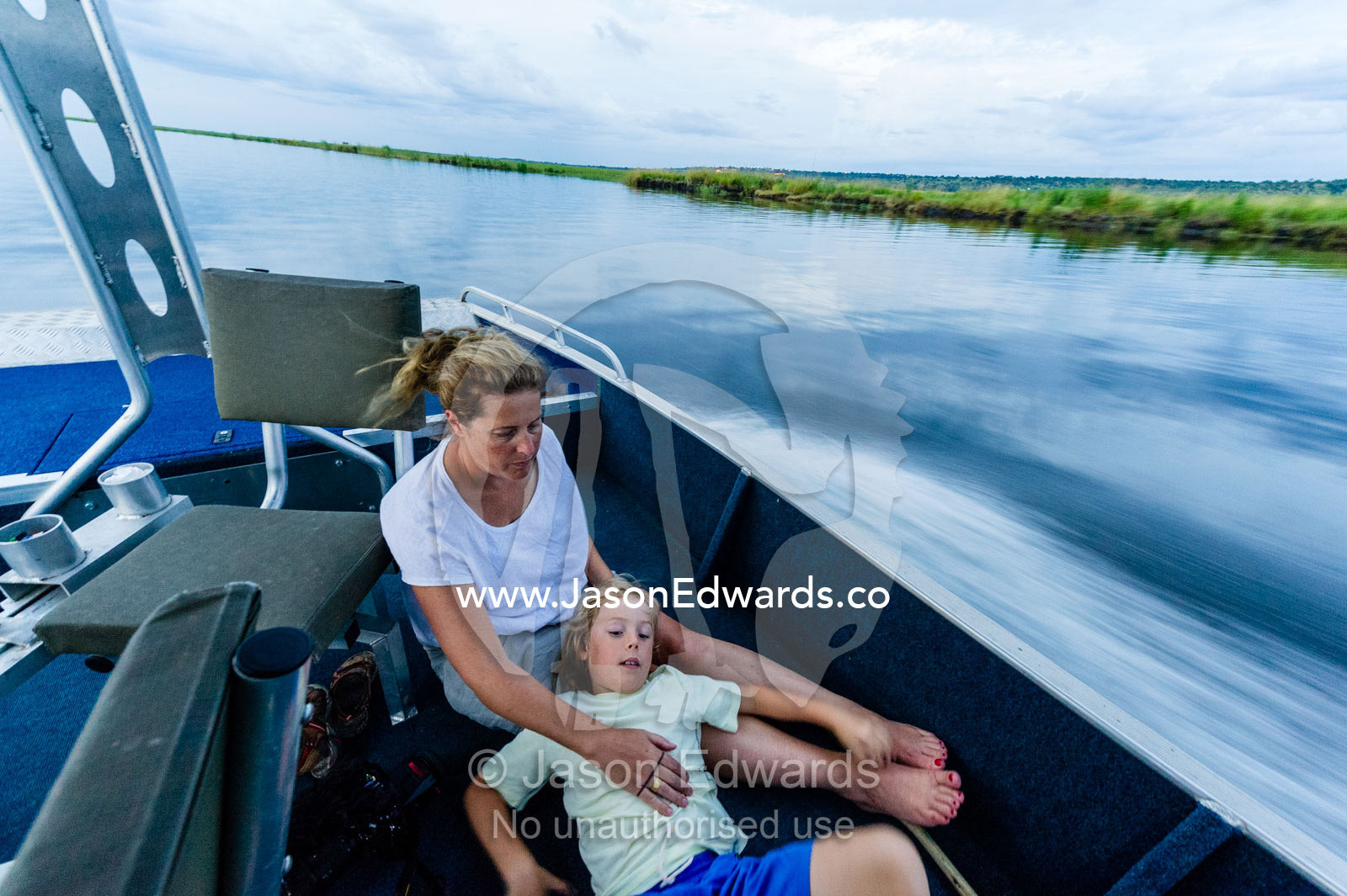 A mother and son resting in a safari boat speeding along a river. Chobe River, Chobe National Park, Botswana.