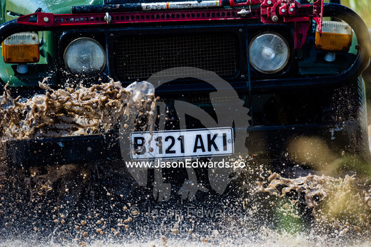 A safari 4wd splashes through the mud of a waterhole. Zarafa Camp, Zibadianja Lagoon, Savute Channel, Linyanti, Botswana.