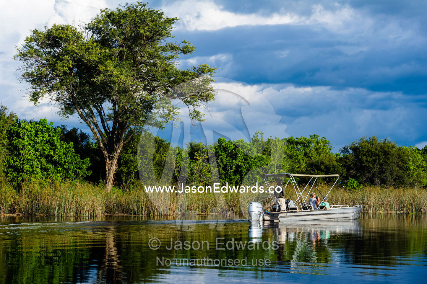 A mother and son watching river wildlife from a safari boat at sunset. Selinda Spillway, Selinda Reserve, Linyanti Region, Northern Botswana.