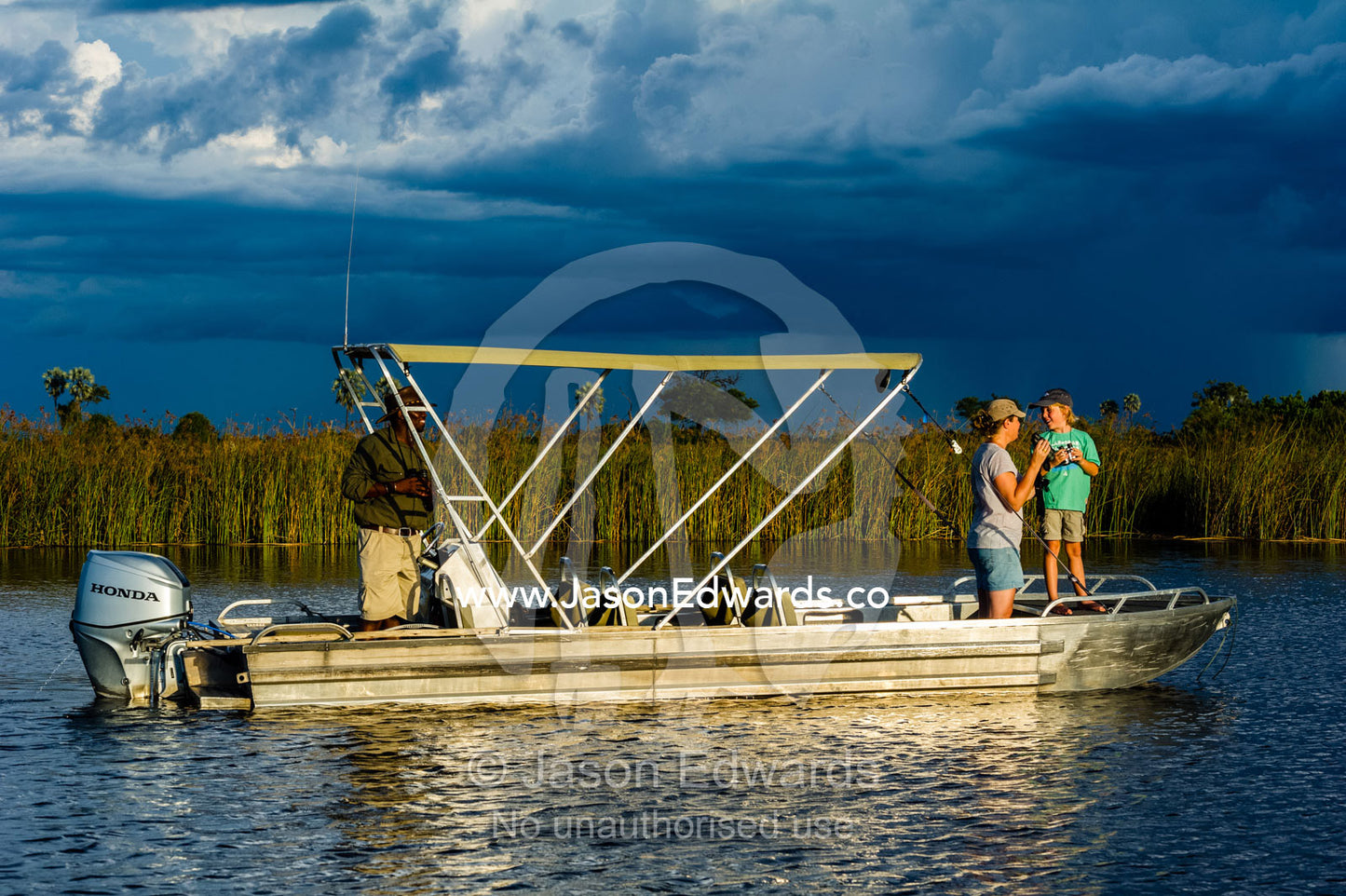 A mother and son watching river wildlife from a safari boat at sunset. Selinda Spillway, Selinda Reserve, Linyanti Region, Northern Botswana.