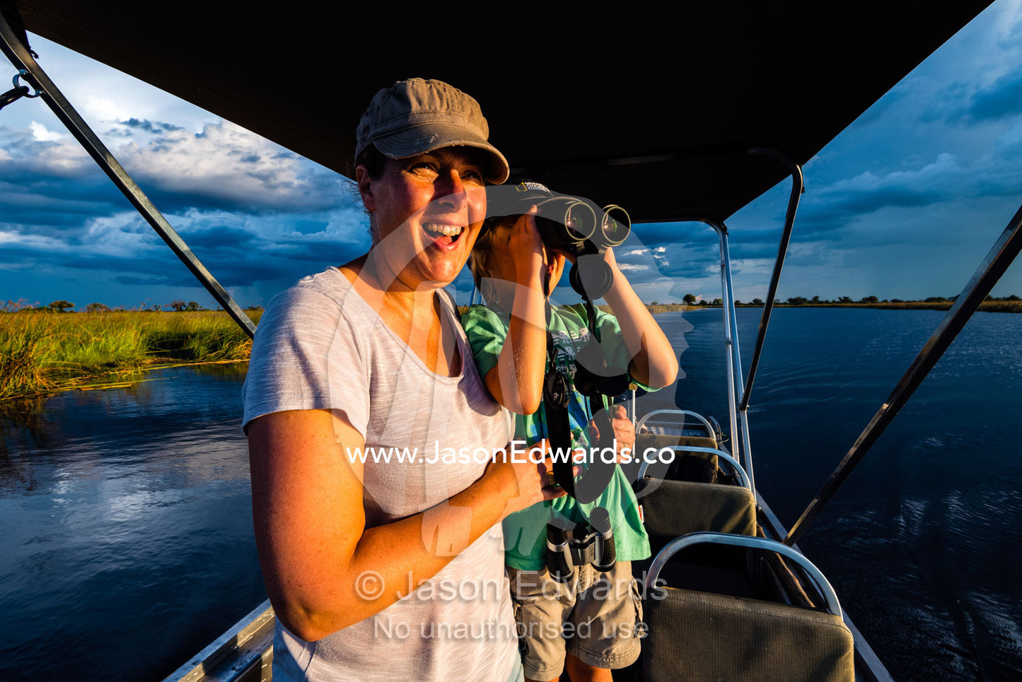 A mother and son watching river wildlife from a safari boat at sunset. Selinda Spillway, Selinda Reserve, Linyanti Region, Northern Botswana.