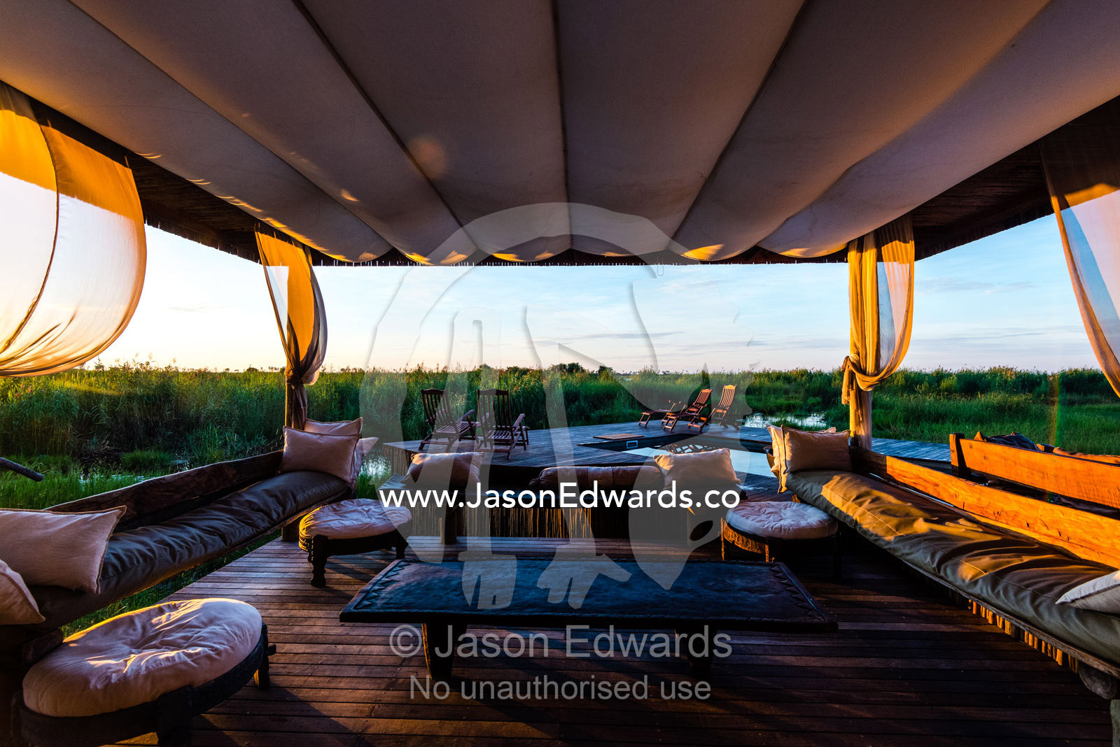 Cushions and sofas in a lounge beneath a canopy in a luxury safari camp. Selinda Camp, Selinda Reserve, Linyanti Region, Northern Botswana.