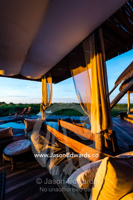 Cushions and sofas in a lounge beneath a canopy in a luxury safari camp. Selinda Camp, Selinda Reserve, Linyanti Region, Northern Botswana.