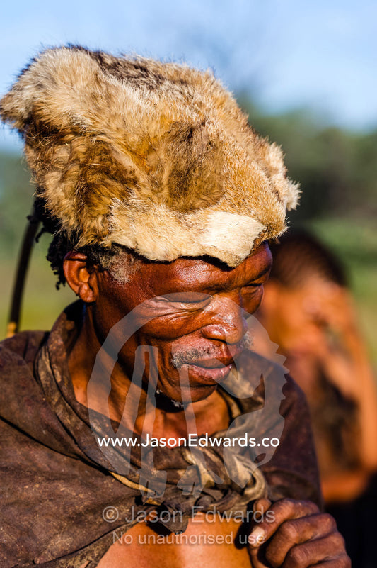 A smiling San Bushmen man wearing the fur of a jackal as a hat and animal skins. Kalahari Desert, Botswana.