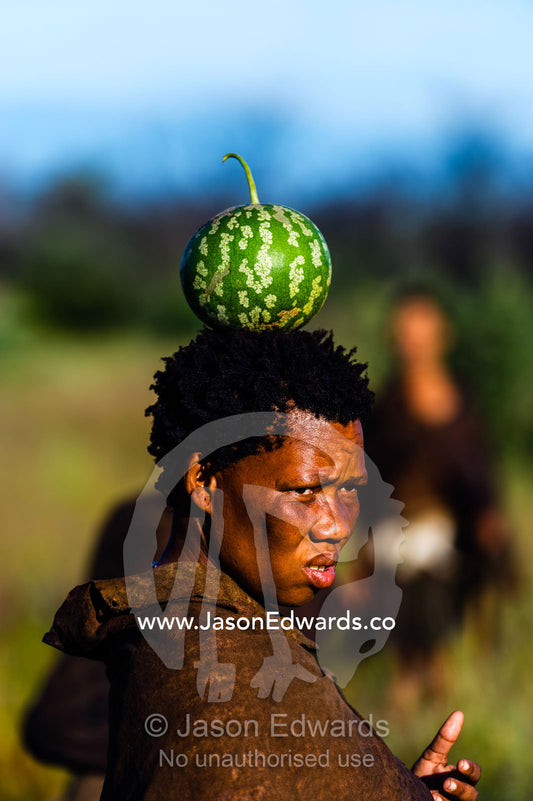 A San Bushmen woman carrying a desert citron melon she found for breakfast on her head. Kalahari Desert, Botswana.