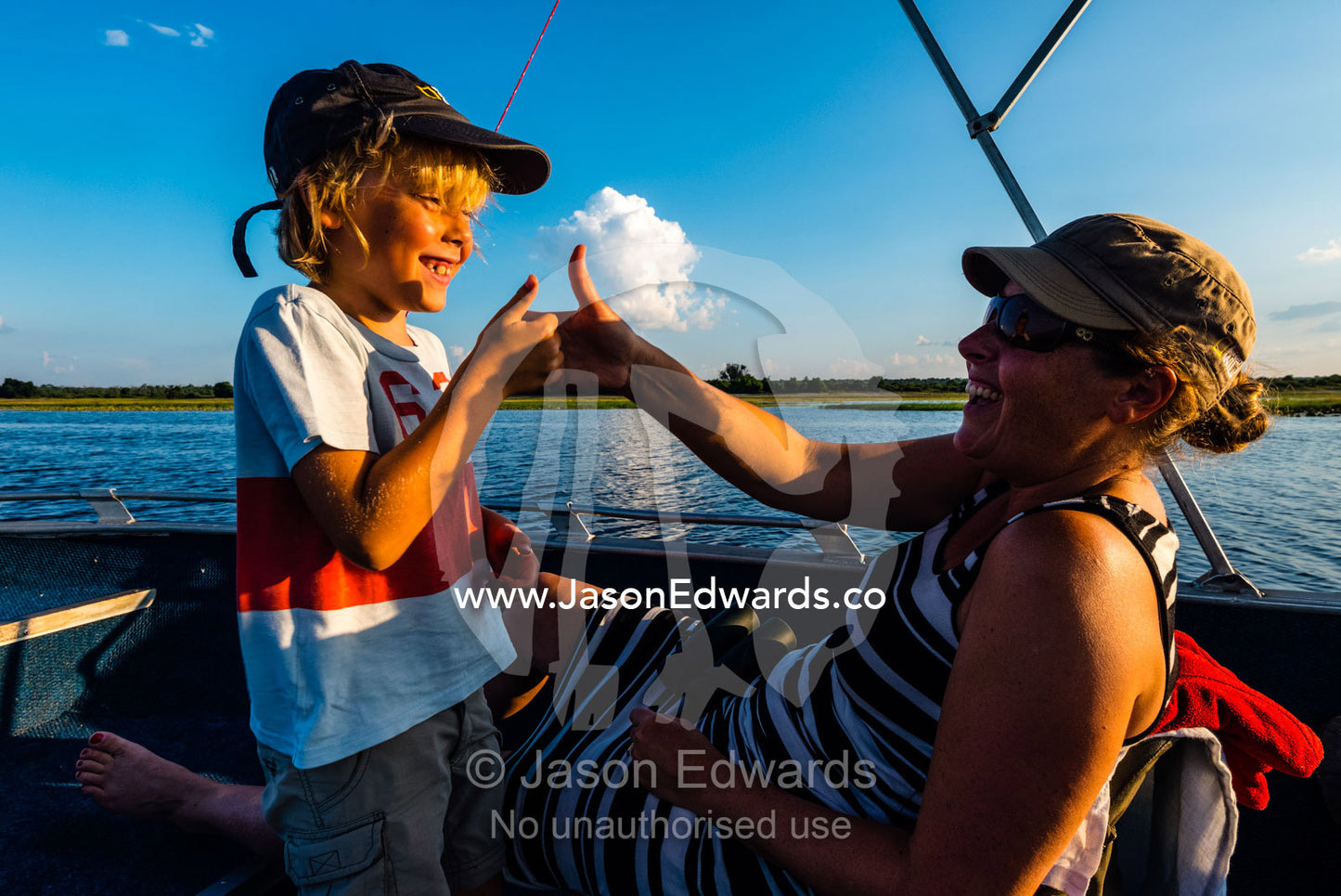 A mother and son playing thumb fighting games on an African safari boat. Chobe River, Chobe National Park, Botswana.