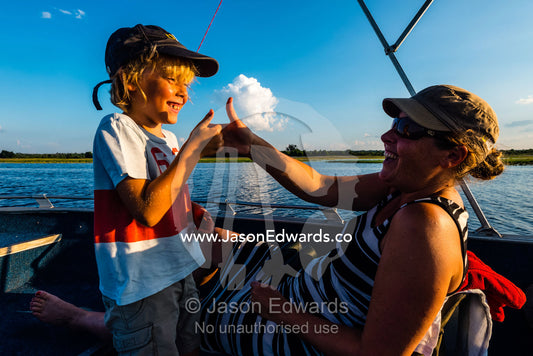 A mother and son playing thumb fighting games on an African safari boat. Chobe River, Chobe National Park, Botswana.