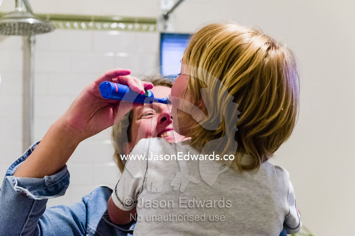 A mother brushes her son's teeth using an electric toothbrush in a bathroom. Carlton North, Melbourne, Victoria, Australia.