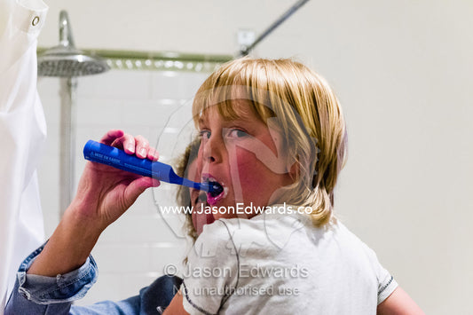A mother brushes her son's teeth using an electric toothbrush in a bathroom. Carlton North, Melbourne, Victoria, Australia.