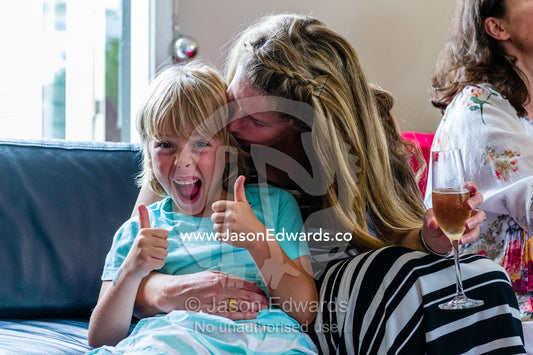 A mother cuddles her son who gives the thumbs-up in celebration. Malvern East, Melbourne, Victoria, Australia.