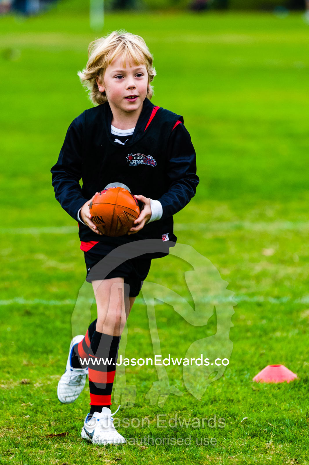 A boy learning to play Australian rules football on a sports field. Edinburgh Gardens, North Fitzroy, Melbourne, Victoria, Australia.