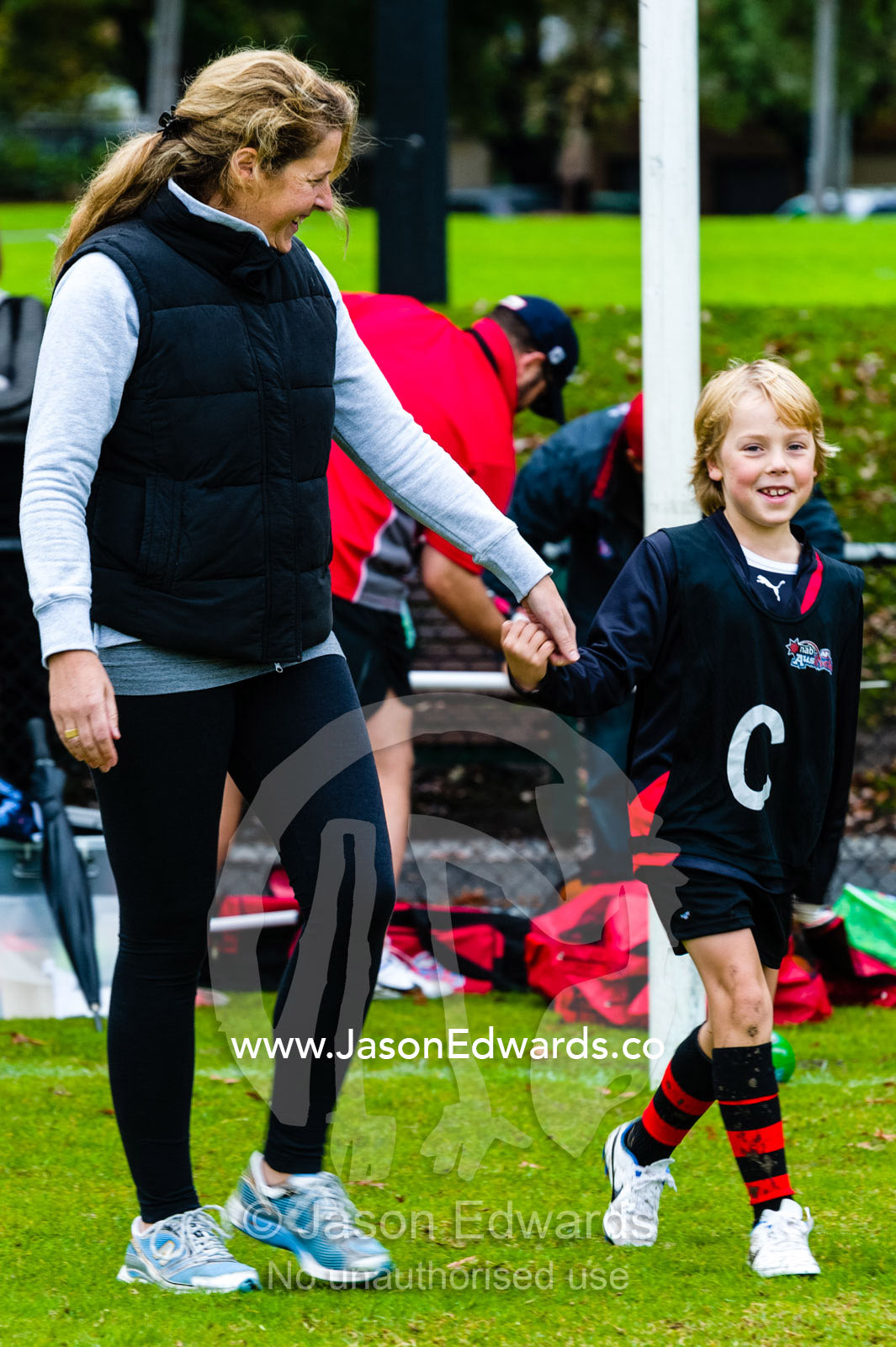 A mother and son learning to play Australian rules football on a sports field. Edinburgh Gardens, North Fitzroy, Melbourne, Victoria, Australia.