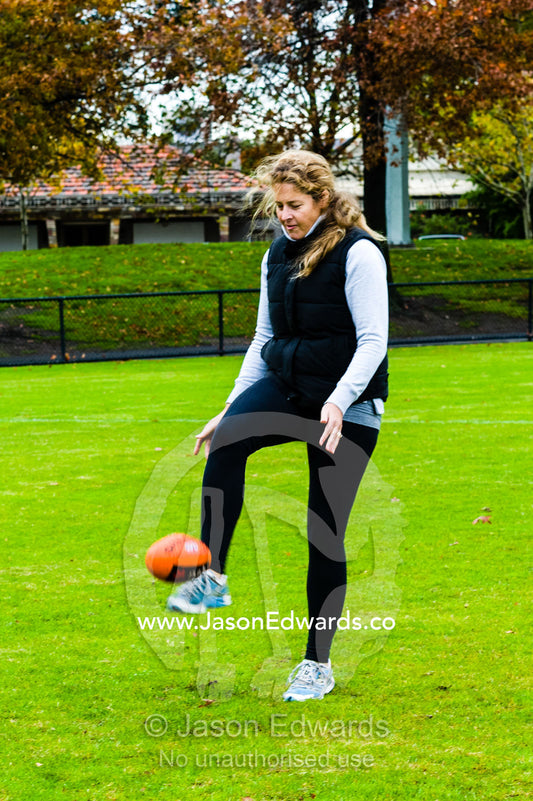 A mother learning to play Australian rules football on a sports field. Edinburgh Gardens, North Fitzroy, Melbourne, Victoria, Australia.