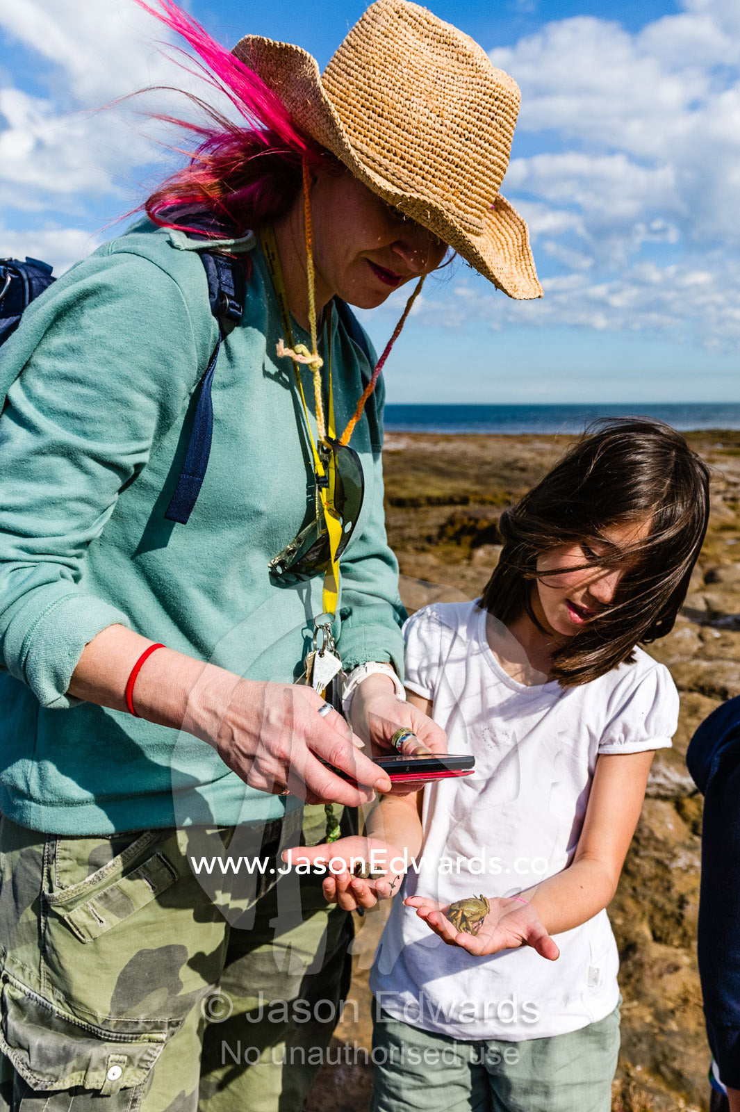 A school teacher photographs ocean specimens with a student on a cell phone. Ricketts Point Marine Sanctuary, Port Phillip Bay, Victoria, Australia.
