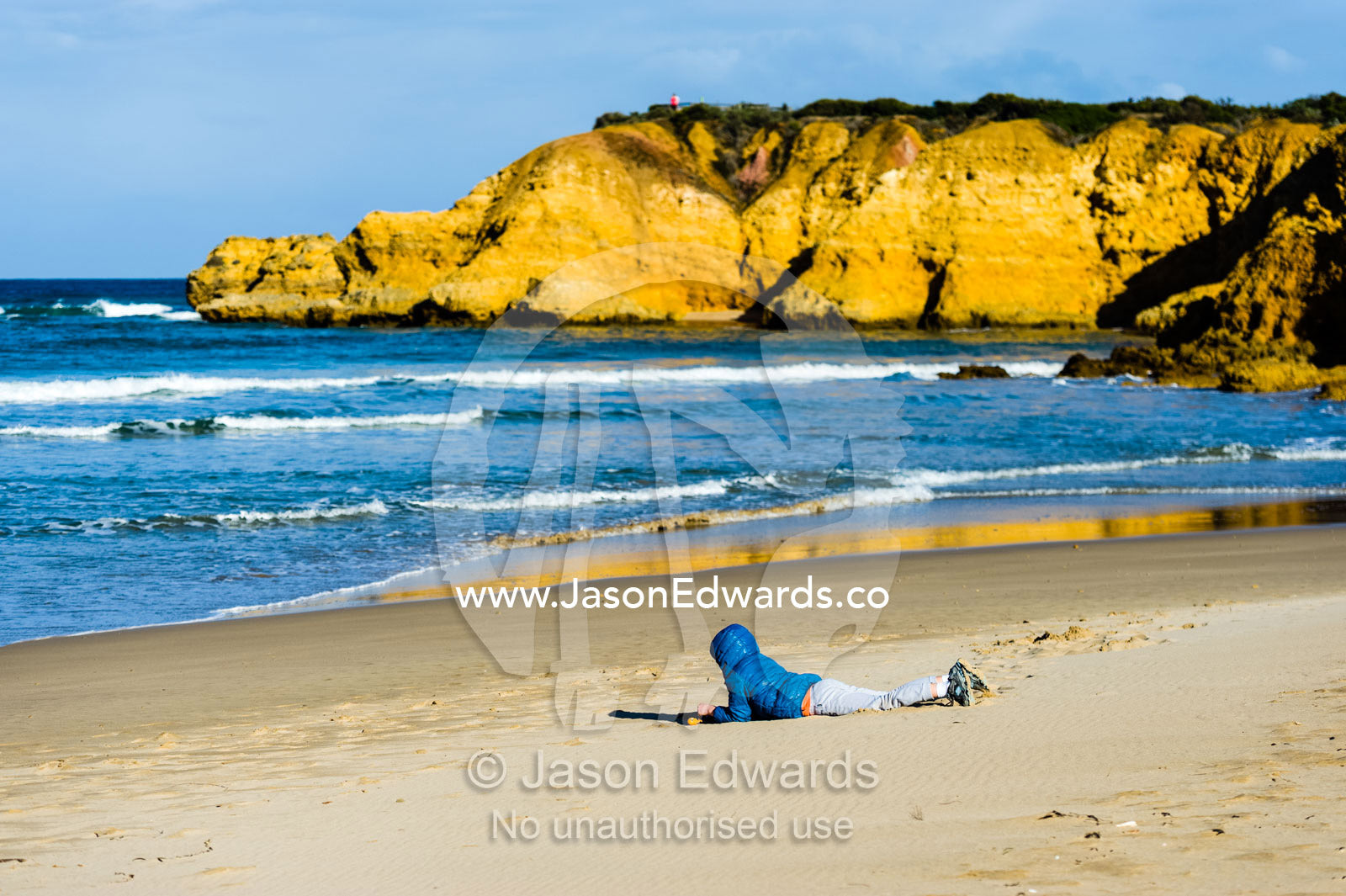 A boy plays on the sand on the beach in winter. Torquay, Surf Coast, Victoria, Australia.