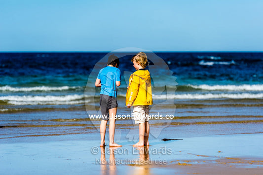 Young friends talking on a beach by the ocean. Torquay, Surf Coast, Victoria, Australia.