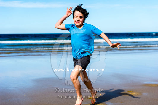 A girl runs along a sandy beach at low tide. Torquay, Surf Coast, Victoria, Australia.