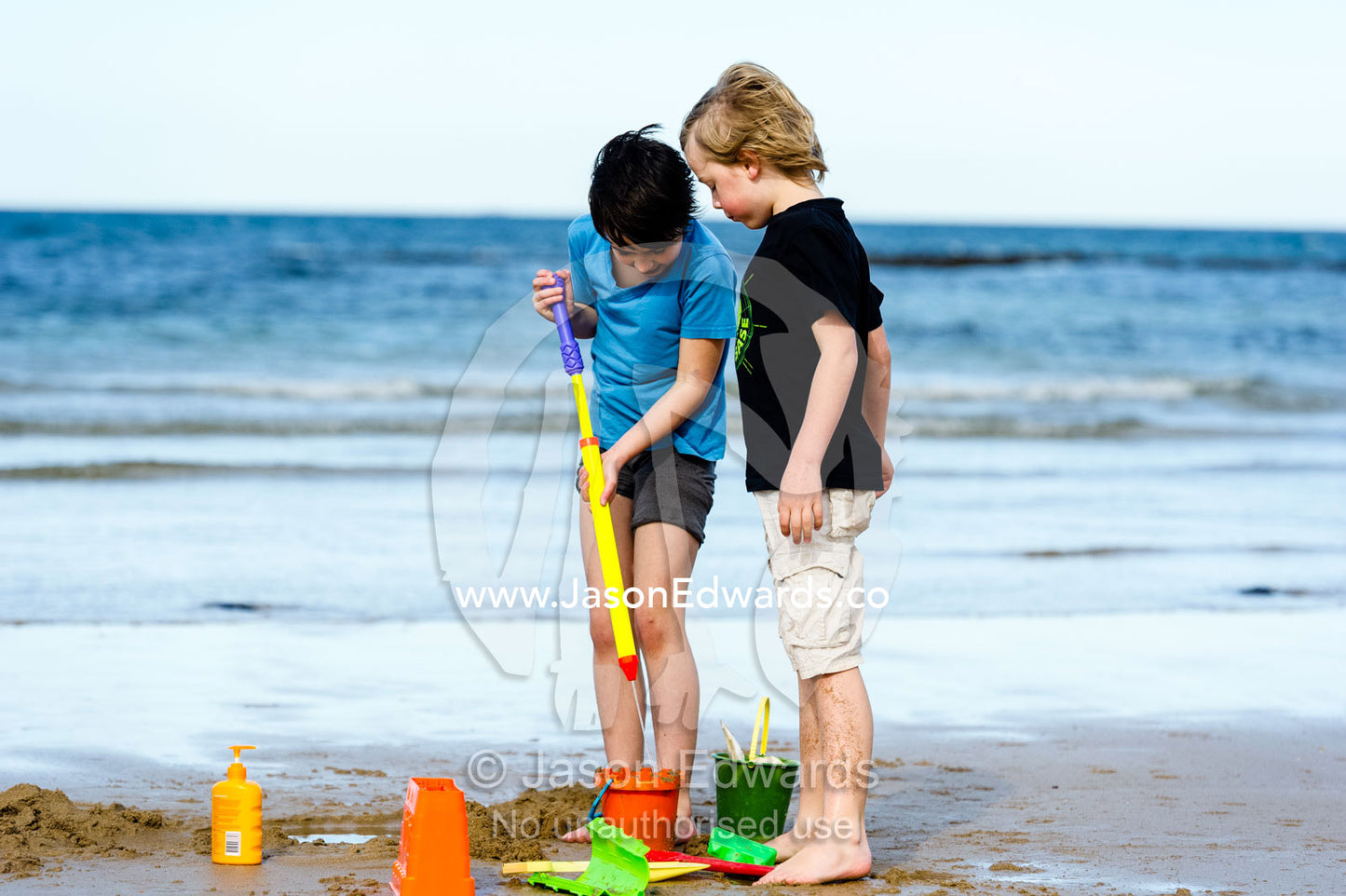 Friends building sand castles on a beach in winter. Torquay, Surf Coast, Victoria, Australia.
