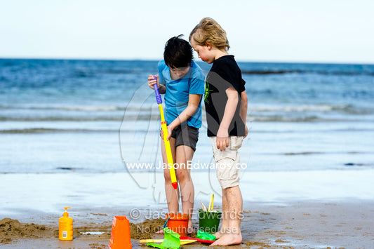 Friends building sand castles on a beach in winter. Torquay, Surf Coast, Victoria, Australia.