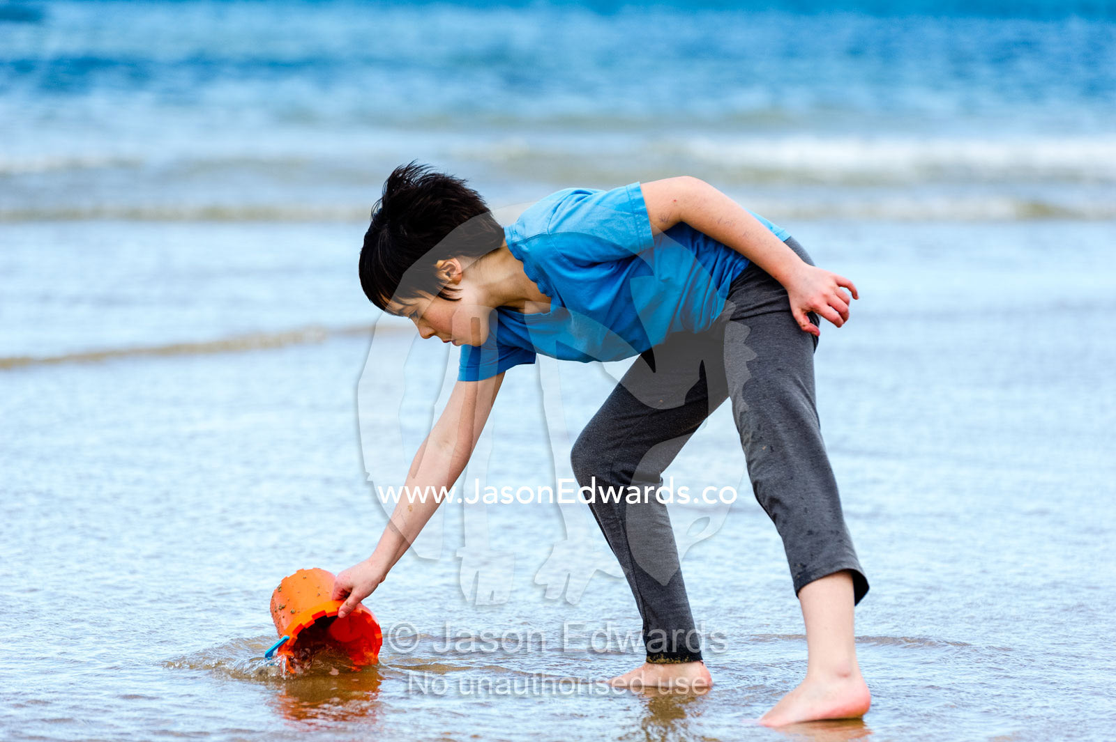 A girl files a bucket with water to make sand castles. Torquay, Surf Coast, Victoria, Australia.