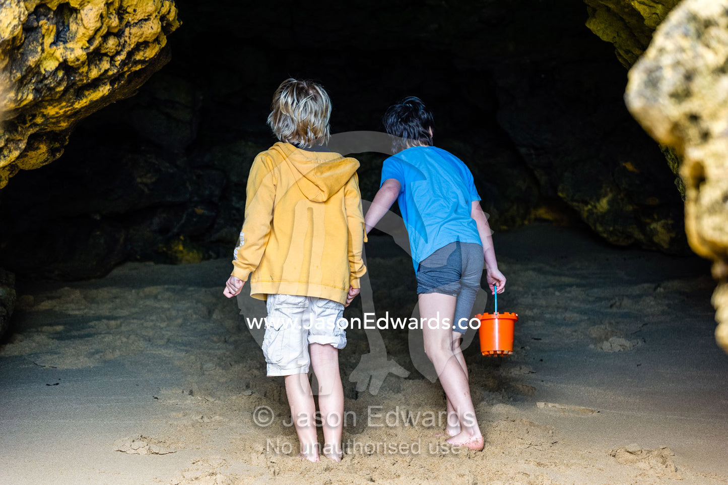 Friends explore a dark cave on a beach at low tide. Torquay, Surf Coast, Victoria, Australia.