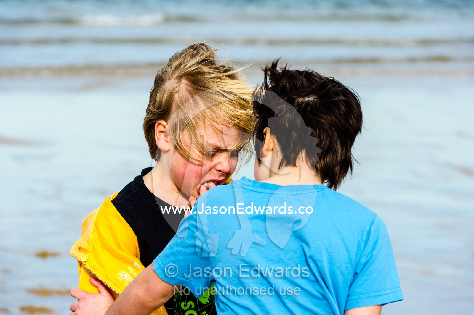A girl comforts her friend who hurt his mouth playing on the beach. Torquay, Surf Coast, Victoria, Australia.
