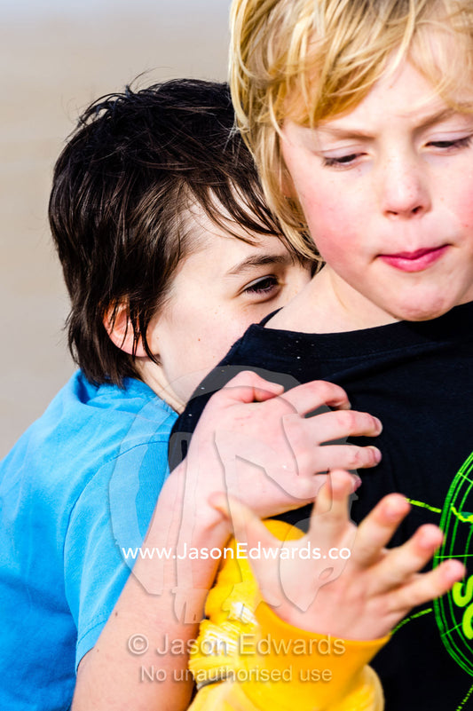 A girl hugs her friend from behind playing on the beach. Torquay, Surf Coast, Victoria, Australia.