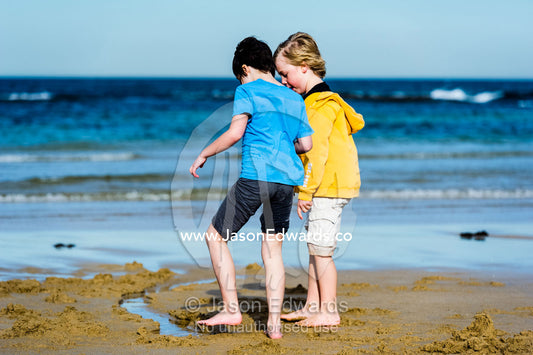 Friends building sand castles on a beach in winter. Torquay, Surf Coast, Victoria, Australia.