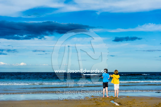 Young friends talking on a beach by the ocean. Torquay, Surf Coast, Victoria, Australia.