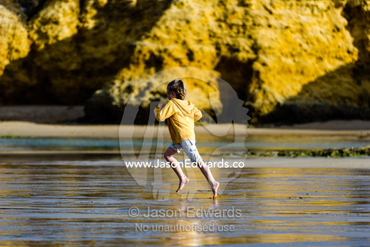 A boy running along the beach at low tide. Torquay, Surf Coast, Victoria, Australia.
