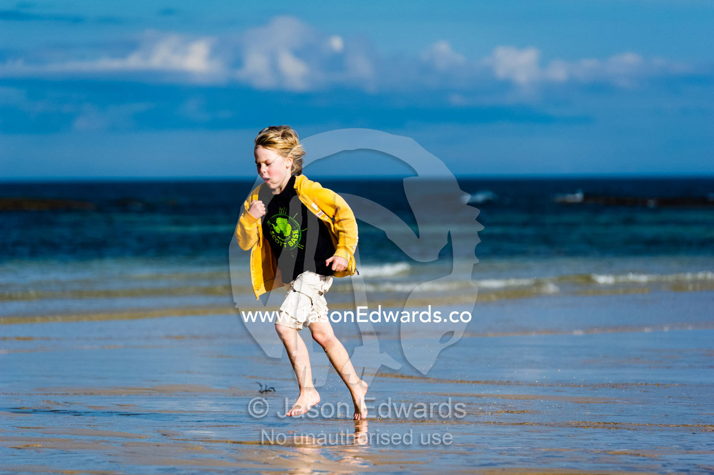 A boy running along the beach at low tide. Torquay, Surf Coast, Victoria, Australia.