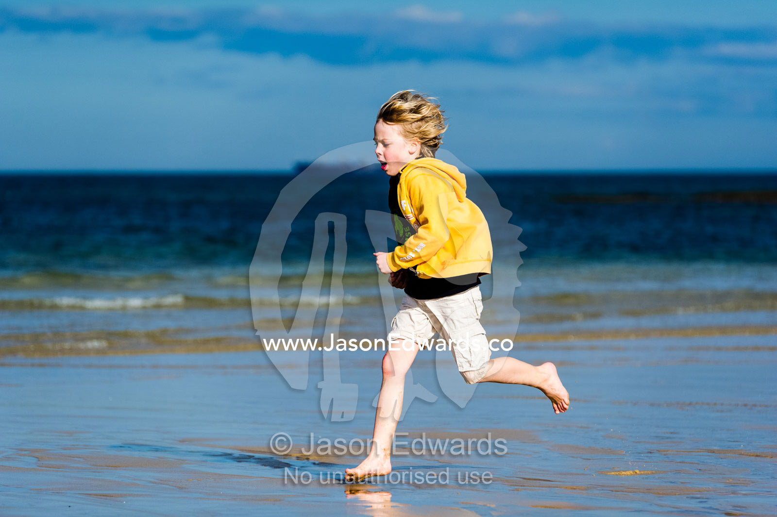 A boy running along the beach at low tide. Torquay, Surf Coast, Victoria, Australia.