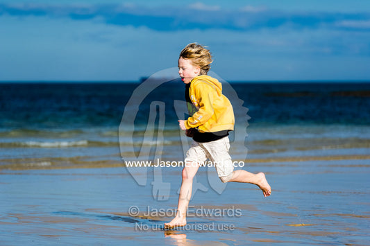 A boy running along the beach at low tide. Torquay, Surf Coast, Victoria, Australia.