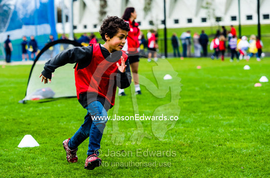 A boy running and playing soccer in a sports field on a school excursion. Albert Park, Melbourne, Victoria, Australia.