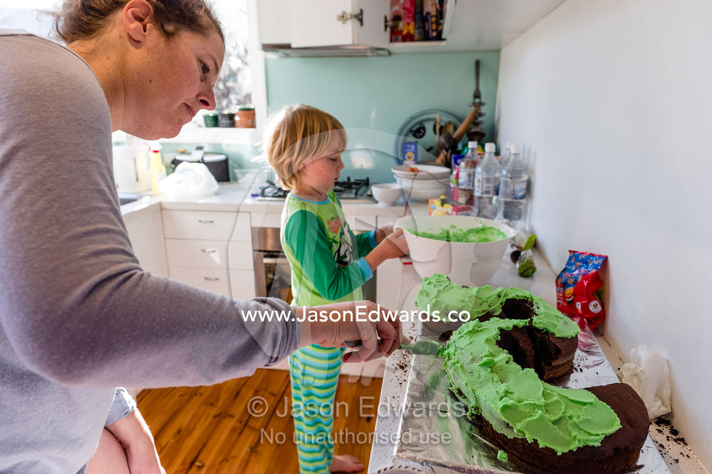 A mother and son decorate a green chocolate snake birthday cake. Carlton North, Melbourne, Victoria, Australia.