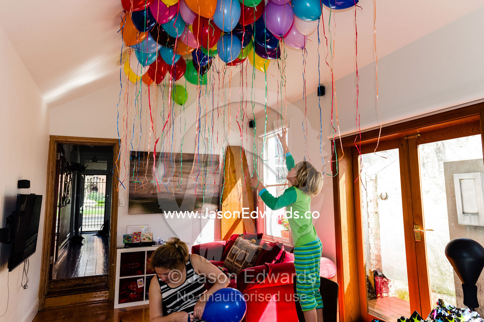 A mother and son inflate colorful helium balloons for a birthday party. Carlton North, Melbourne, Victoria, Australia.